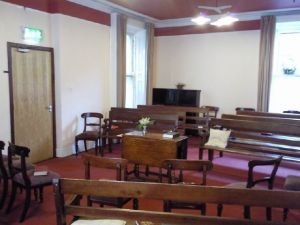 interior photo of Eustace Street Meeting House where Meeting for Worship takes place. Furnished with benches and chairs facing a table in the middle of the room.